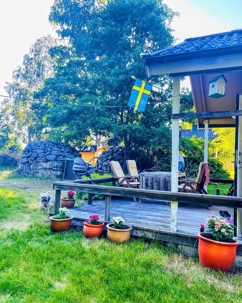 Deck with garden chairs and flower pots on the lawn outside Stuga Eos in summer