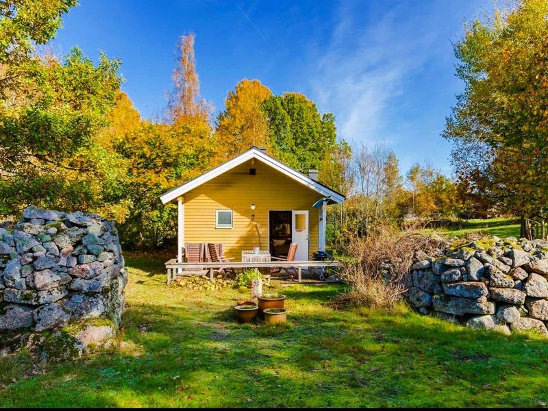 Yellow Stuga Eos cabin with its deck, between old stone walls in autumn, Holmsjö